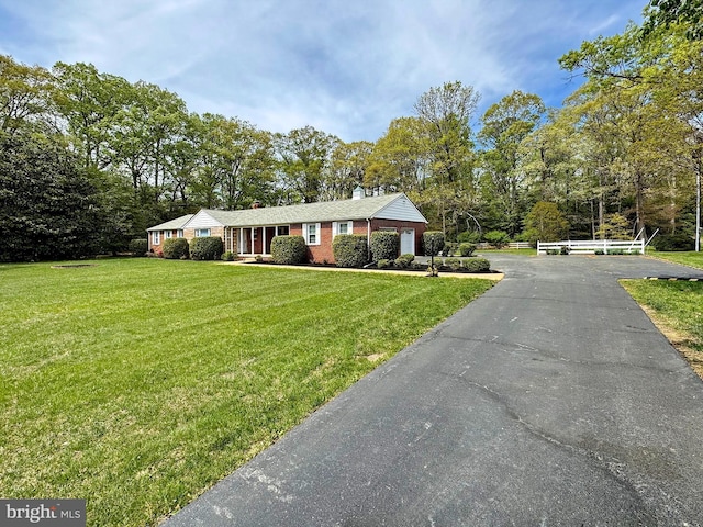 ranch-style home with a chimney, brick siding, aphalt driveway, a garage, and a front lawn
