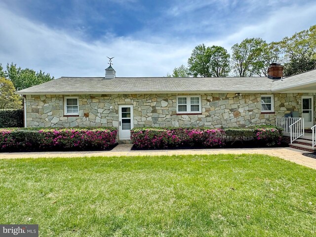 ranch-style home with a front lawn, stone siding, and a chimney