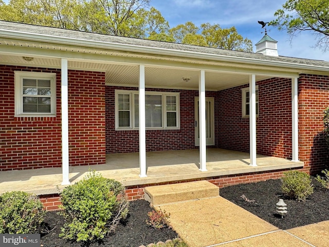 doorway to property with covered porch and brick siding