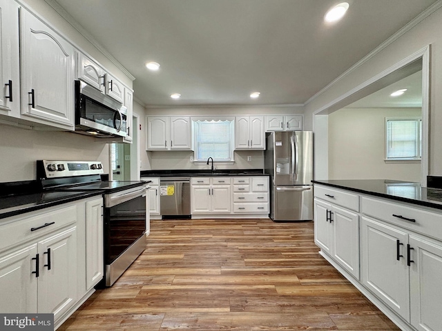 kitchen with white cabinetry, crown molding, appliances with stainless steel finishes, dark countertops, and light wood-type flooring