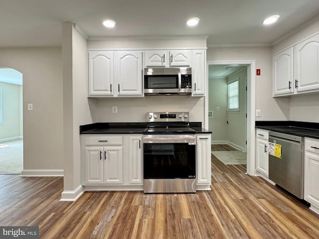 kitchen with white cabinetry, appliances with stainless steel finishes, dark countertops, light wood-style floors, and arched walkways