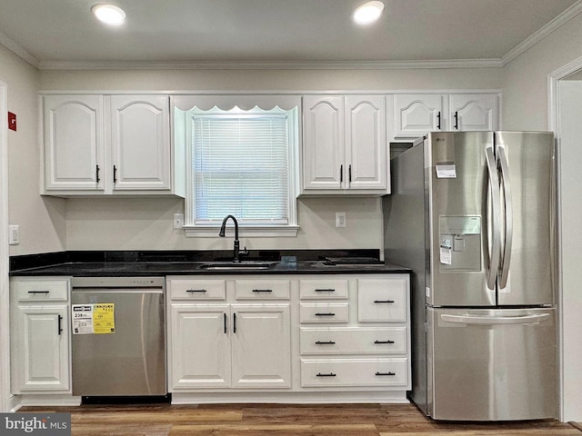 kitchen featuring crown molding, white cabinets, a sink, appliances with stainless steel finishes, and dark countertops