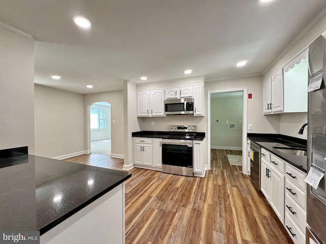 kitchen featuring appliances with stainless steel finishes, light wood-style flooring, white cabinets, and arched walkways