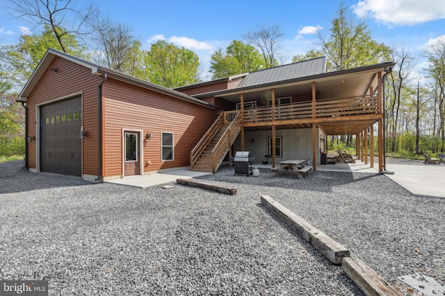 back of house featuring stairway, a deck, an attached garage, driveway, and a patio