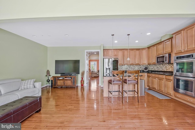 kitchen featuring a breakfast bar area, tasteful backsplash, light wood-type flooring, open floor plan, and stainless steel appliances