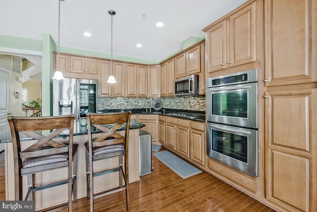 kitchen with light brown cabinets, stainless steel appliances, wood finished floors, backsplash, and pendant lighting