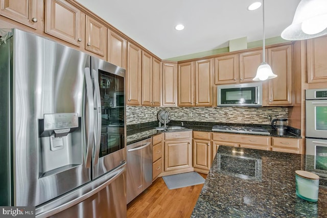 kitchen with a sink, appliances with stainless steel finishes, hanging light fixtures, and decorative backsplash
