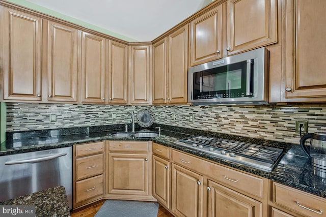 kitchen with backsplash, stainless steel appliances, a sink, and dark stone counters