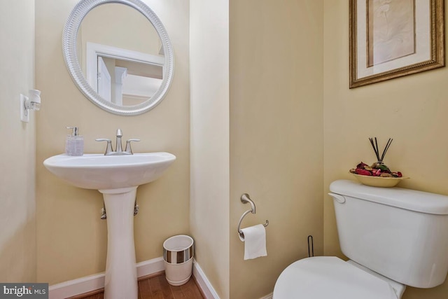half bathroom featuring toilet, baseboards, a sink, and wood finished floors