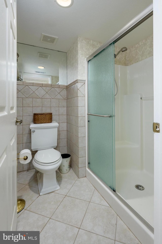 bathroom featuring visible vents, tile walls, tile patterned flooring, a stall shower, and toilet