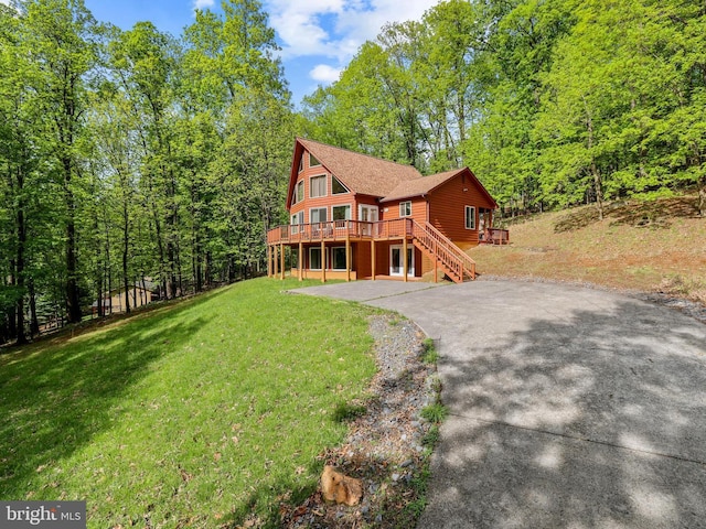 chalet / cabin featuring asphalt driveway, a wooden deck, a front yard, stairs, and a wooded view