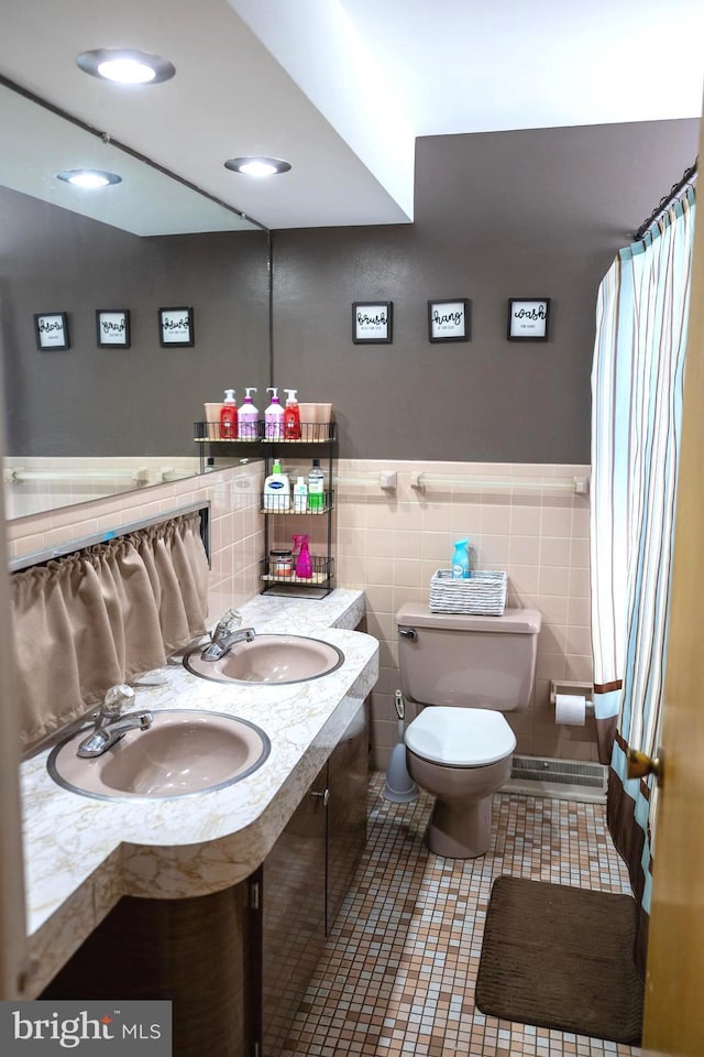 full bathroom with toilet, tile walls, a sink, and double vanity