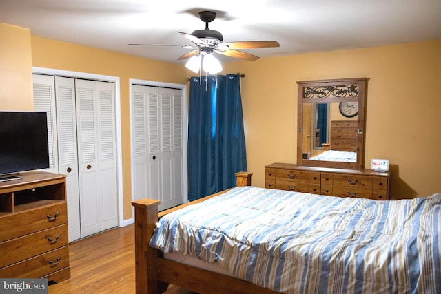 bedroom with wood finished floors, ceiling fan, and two closets