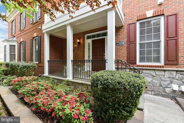 doorway to property featuring a porch, stone siding, and brick siding