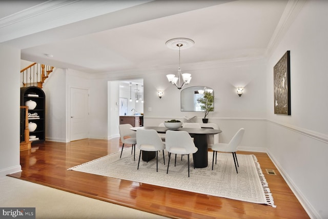 dining room with wood finished floors, visible vents, crown molding, and a notable chandelier