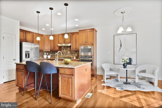 kitchen featuring tasteful backsplash, brown cabinetry, stainless steel appliances, and light wood-style floors
