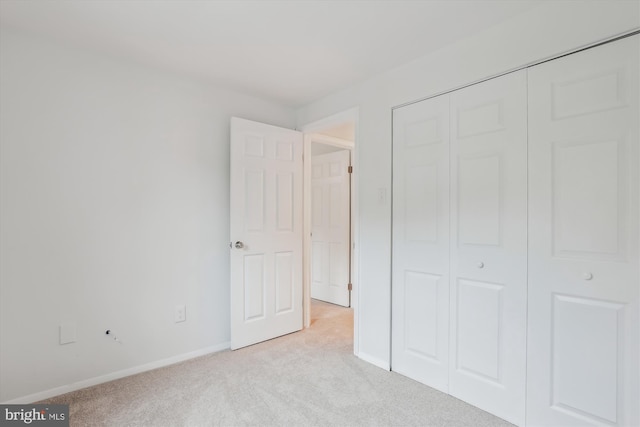 unfurnished bedroom with a closet, light colored carpet, and baseboards