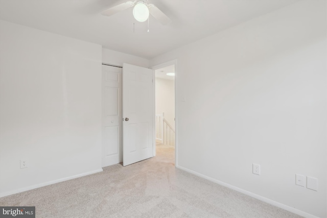 unfurnished bedroom with light colored carpet, a ceiling fan, and baseboards