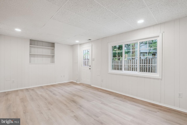 empty room with built in shelves, recessed lighting, wood finished floors, and baseboards