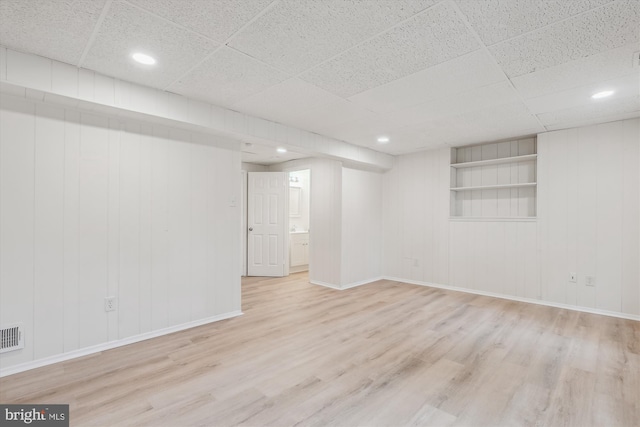 finished basement with a paneled ceiling, visible vents, wood finished floors, and baseboards