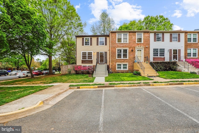 townhome / multi-family property featuring brick siding, fence, a front lawn, and uncovered parking