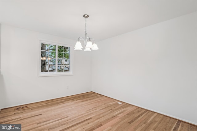 spare room with a chandelier, visible vents, and wood finished floors