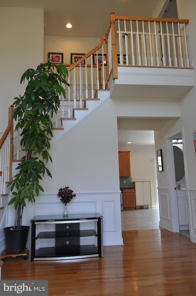 stairs with wood finished floors, a high ceiling, and a decorative wall
