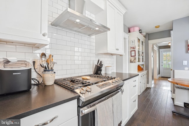 kitchen with dark countertops, white cabinets, stainless steel gas range oven, and wall chimney range hood