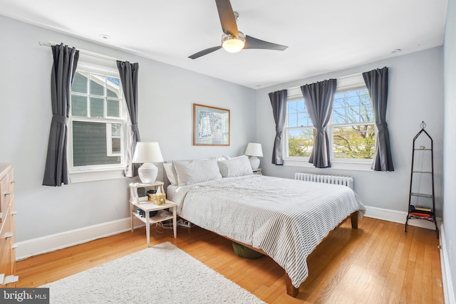 bedroom with radiator, multiple windows, baseboards, and hardwood / wood-style floors