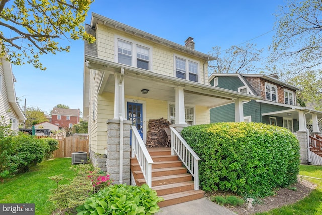 american foursquare style home with fence, covered porch, a chimney, and central AC