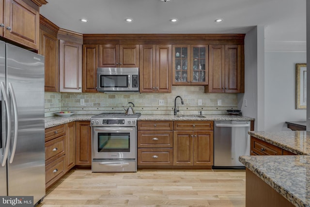 kitchen with a sink, appliances with stainless steel finishes, brown cabinetry, and tasteful backsplash