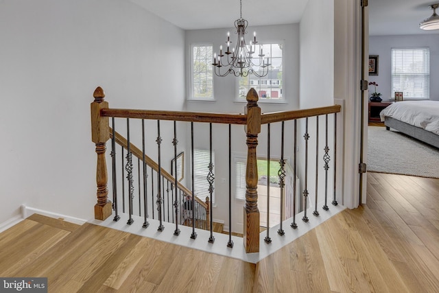 stairs with a chandelier, a wealth of natural light, wood finished floors, and baseboards