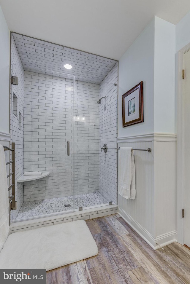 full bathroom with a stall shower, a wainscoted wall, and wood finished floors