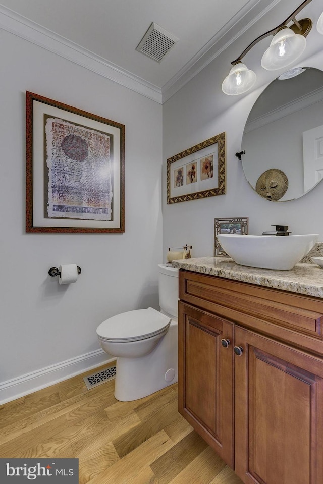 half bathroom with visible vents, wood finished floors, toilet, and crown molding