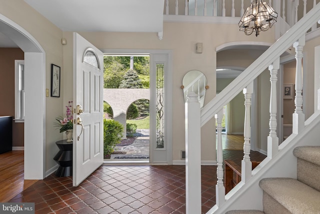 entrance foyer featuring stairs, arched walkways, a chandelier, and baseboards
