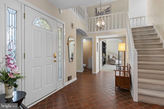 foyer entrance featuring arched walkways, stairway, a chandelier, dark tile patterned floors, and baseboards