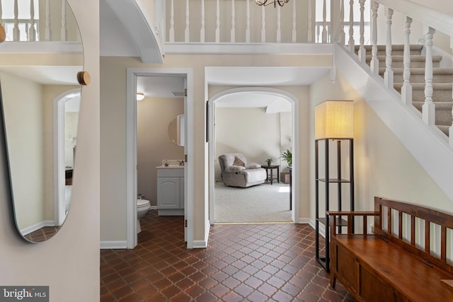 entryway featuring arched walkways, a high ceiling, dark carpet, baseboards, and dark tile patterned flooring