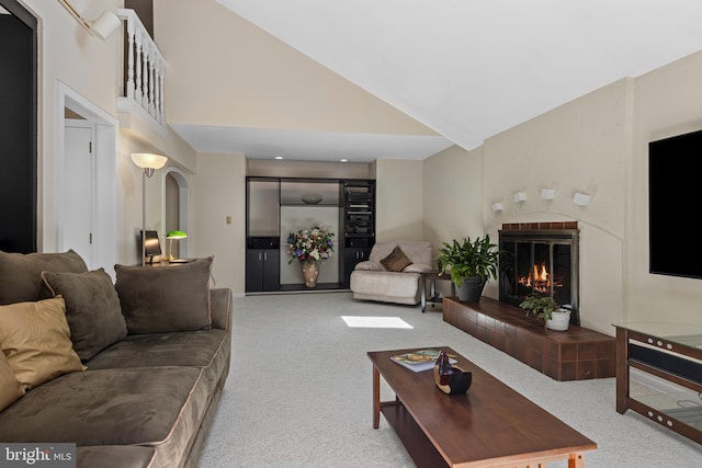 living room featuring carpet flooring, a glass covered fireplace, high vaulted ceiling, and arched walkways