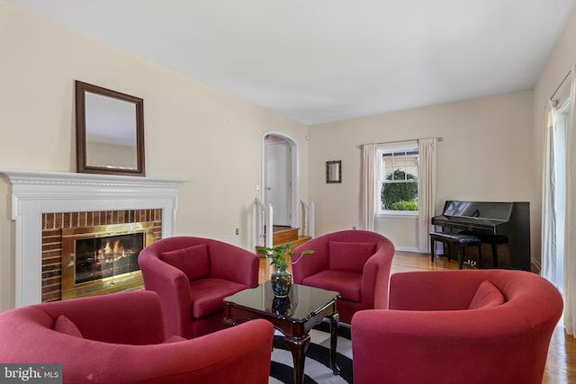 living room with a brick fireplace, wood finished floors, and arched walkways