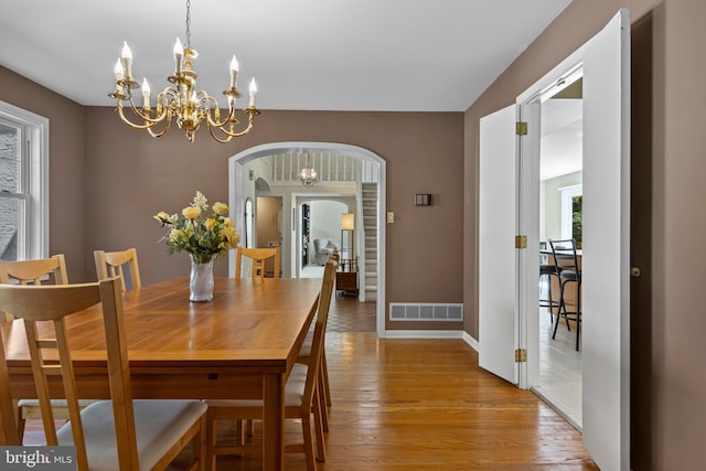 dining area featuring a chandelier, arched walkways, wood finished floors, and baseboards