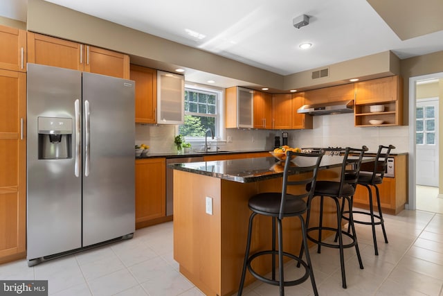 kitchen with stainless steel appliances, a center island, light tile patterned flooring, a kitchen bar, and backsplash
