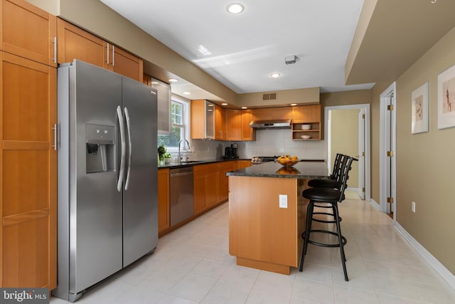 kitchen with stainless steel appliances, extractor fan, a sink, a breakfast bar, and backsplash