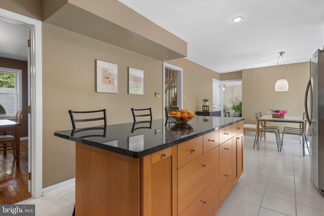 kitchen with freestanding refrigerator, baseboards, dark stone countertops, a center island, and light tile patterned floors