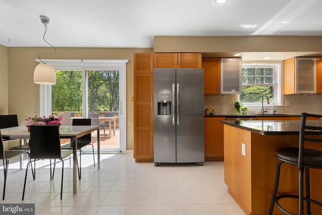 kitchen featuring stainless steel fridge, brown cabinetry, a sink, backsplash, and glass insert cabinets