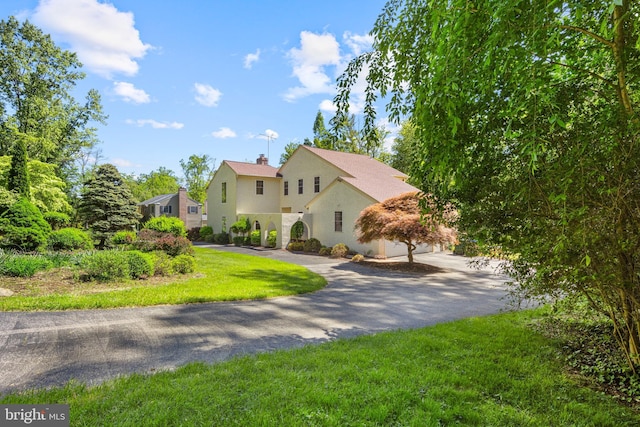 view of front of property featuring stucco siding, a front lawn, asphalt driveway, and a chimney