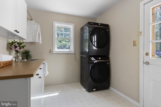 laundry room with estacked washer and dryer, cabinet space, light floors, and healthy amount of natural light