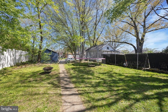 view of yard featuring a fenced backyard, a trampoline, and a fire pit