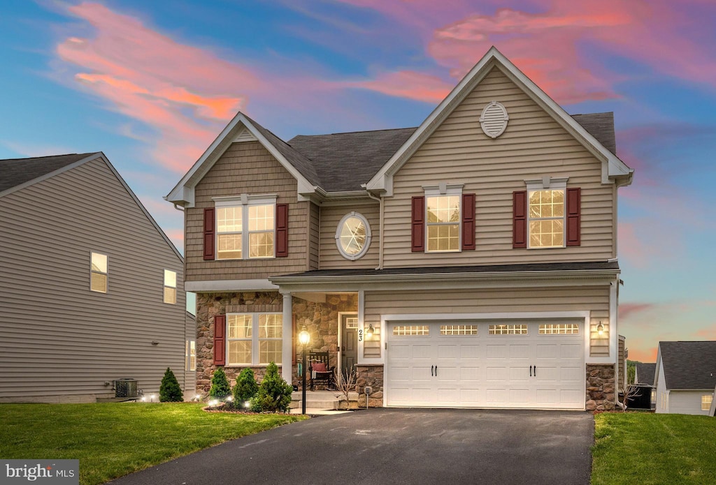 traditional-style house featuring a front lawn, central air condition unit, a garage, stone siding, and aphalt driveway