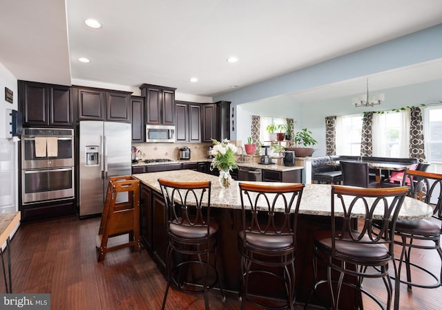 kitchen with stainless steel appliances, light stone countertops, dark wood-style floors, and a center island
