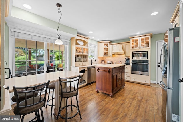 kitchen with a kitchen island, appliances with stainless steel finishes, wood finished floors, light countertops, and custom range hood